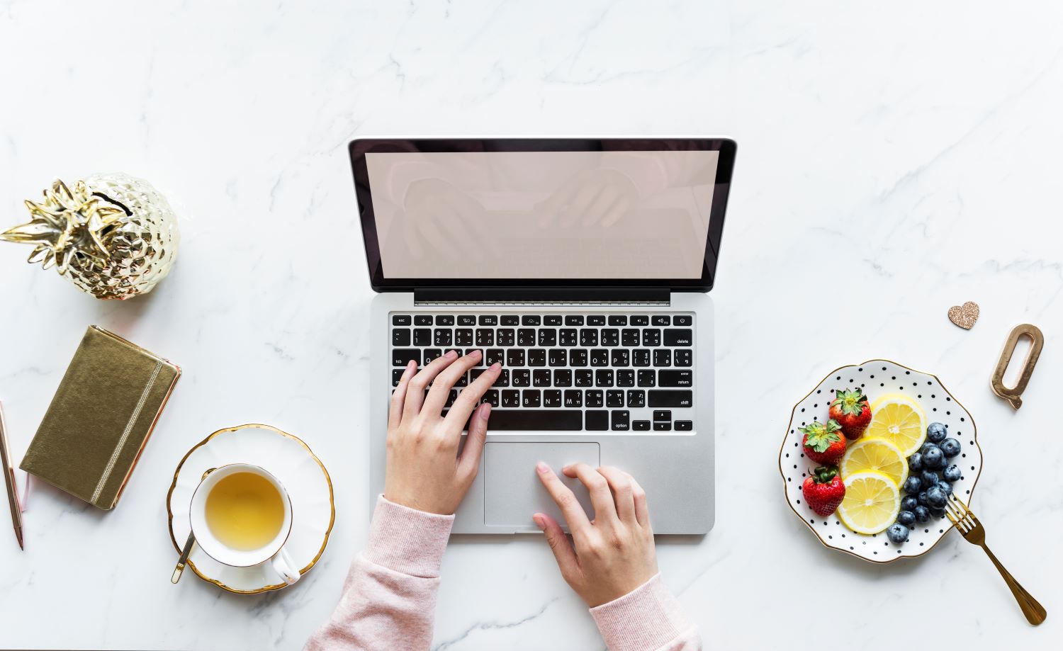 Frau, die am Laptop schreibt, daneben Obst und Tee